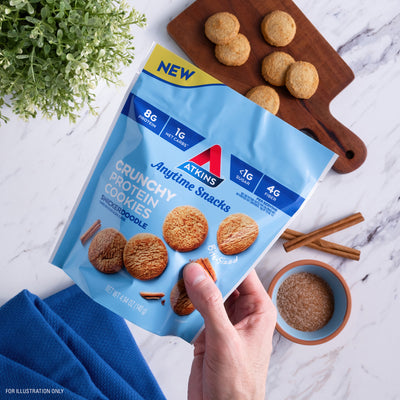 Holding snickerdoodle Bite-Sized Crunchy Protein Cookies with marble table at the background with cookies and a bowl of cinnamon sugar.